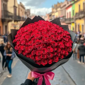 Foto de ramo buchon con rosas rojas y papel negro con moño rosa. Calle de fondo